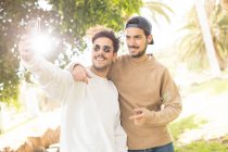 Sorridenti amici maschi felici scattare selfie con smartphone nel parco soleggiato — Foto stock