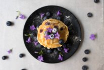 Stack of appetizing tasty crumpets with blueberries and purple flowers on black plate — Stock Photo