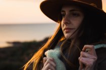 Мечтательная молодая женщина в шляпе стоит на берегу моря и смотрит в сторону — стоковое фото