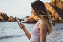 Woman in sportswear standing at seaside and browsing smartphone — Stock Photo