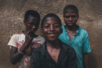 Kamerun - Afrika - 5. April 2018: fröhliche harte afrikanische Jungs stehen an einer rauen Mauer und blicken in die Kamera — Stockfoto