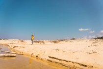 Donna in cappello in piedi sulla riva sabbiosa sotto il cielo blu — Foto stock