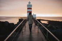 Back view of woman walking to the lighthouse at seaside in the evening. — Stock Photo