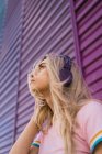 Молода жінка з фіолетовими навушниками, що стоять на фіолетовій стіні — стокове фото