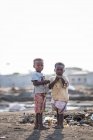 ANGOLA - ÁFRICA - 5 DE ABRIL DE 2018 - Dos chicos parados en el basurero y mirando a la cámara en el pueblo - foto de stock