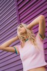 Mujer joven con auriculares morados de pie contra la pared morada - foto de stock