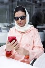 Moroccan woman with hijab and traditional Arabic dress using mobile phone in cafe — Stock Photo