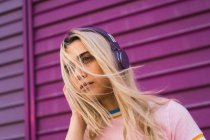 Junge Frau mit lila Kopfhörern steht vor lila Wand — Stockfoto
