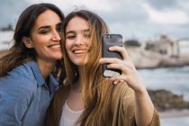 Mulher sorridente e adolescente tomando selfie na praia — Fotografia de Stock