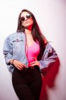 Young pink dressed woman in sunglasses standing at white wall and looking at camera — Stock Photo