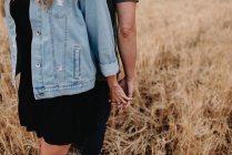 Crop couple standing back to back and holding hands on dry field. — Stock Photo