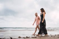 Elegant woman and teen girl walking on beach together — Stock Photo