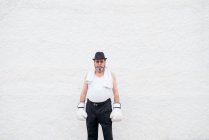 Adult man in hat and white boxing gloves at rough wall. — Stock Photo