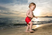 Маленький мальчик прогуливается по песчаному пляжу на закате — стоковое фото
