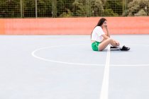Jovem mulher sentada em terreno desportivo — Fotografia de Stock