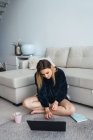 Casual donna bionda utilizzando il computer portatile mentre seduto sul pavimento a casa — Foto stock