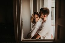 Feliz jovem casal abraçando na janela em casa — Fotografia de Stock