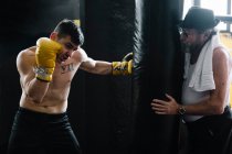 Взрослый тренер, стоящий и держащий в руках боксерскую грушу для спортсмена в спортзале. — стоковое фото
