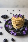 Stapel leckerer Knollen mit Blaubeeren und lila Blüten auf schwarzem Teller — Stockfoto