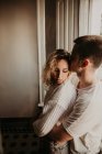 Romantic young couple embracing at window at home — Stock Photo
