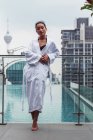 Frau im Bademantel steht am Pool in moderner Stadt — Stockfoto