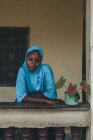 Kamerun - Afrika - 5. April 2018: Hübsche junge Afrikanerin in blauer traditioneller Kleidung lehnt am Geländer und blickt in die Kamera — Stockfoto
