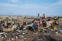 ANGOLA - AFRICA - APRIL 5, 2018 - African children standing and playing on grungy car on the dump — Stock Photo