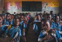 КАМЕРУН - Африка - 5 апреля 2018 года: африканские ученики сидят с карандашами в классе и смотрят в камеру — стоковое фото