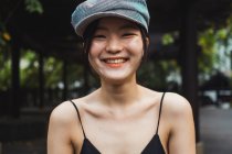 Retrato de sonriente joven asiática en gorra en parque - foto de stock