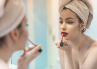 Giovane donna in topless con trucco e asciugamano sulla testa applicare il rossetto davanti allo specchio in bagno — Foto stock