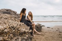 Mujer y adolescente chica sentada en la roca en la playa y hablando - foto de stock