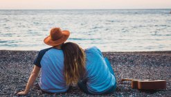 Uomo e donna seduti con la chitarra sulla spiaggia al mare — Foto stock