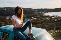 Frau mit Karte sitzt auf Autodach an Küste — Stockfoto