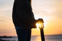 Woman in jacket standing with guitar at seaside at sunset — Stock Photo