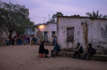 АНГОЛА - Африка - 5 апреля 2018 года - Этнические люди, стоящие и сидящие на деревенской улице в грандиозных домах вечером — стоковое фото
