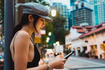Femme asiatique dans des vêtements élégants en utilisant smartphone sur la rue en ville — Photo de stock