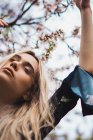 Young blonde woman with closed eyes standing at blooming tree — Stock Photo