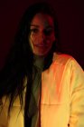 Красива молода жінка в білій куртці зі світлими плямами на обличчі дивиться на камеру на темному фоні — стокове фото