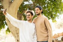 Улыбающиеся счастливые друзья-мужчины делают селфи со смартфоном в солнечном парке — стоковое фото
