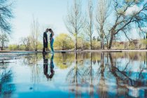Girls standing head to head and reflecting in huge puddle in spring park — Stock Photo