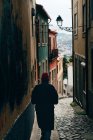 Вид сзади человека в красной шляпе, идущего по узкой улочке в старом городе, Порту, Португалия — стоковое фото