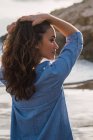 Женщина с длинными каштановыми волосами стоит на пляже с поднятыми руками — стоковое фото