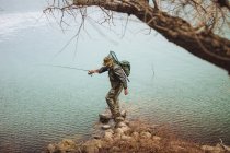 Pescador de pie con la barra y el equilibrio en la roca en el lago - foto de stock