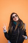 Excited woman showing victory sign against orange wall — Stock Photo