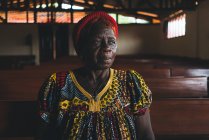 КАМЕРУН - Африка - 5 апреля 2018 года: Старшая африканская женщина в традиционной одежде стоит в церкви и смотрит в сторону — стоковое фото