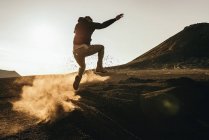 Неузнаваемый человек прыгает по сухой пыльной земле на склоне холма. — стоковое фото