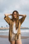 Portrait of teenage girl with long hair standing on beach with hands behind head — Stock Photo