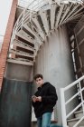 Молодой красивый мужчина стоит на потрепанной лестнице и держит в руках мобильный телефон — стоковое фото