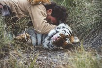 Man stroking tiger while lying in grass — Stock Photo