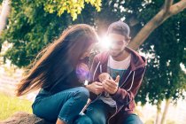 Riendo joven pareja sentado con teléfono inteligente en el parque - foto de stock